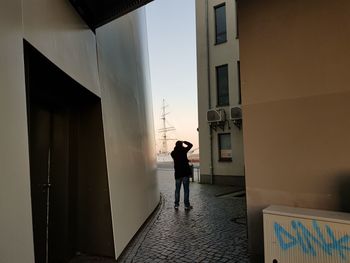 Rear view of silhouette man standing by building against sky