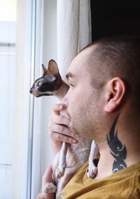 Side view of man with cat standing by window at home