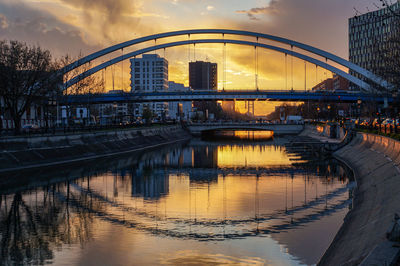 Bridge over river in city against sky during sunset