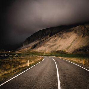 Empty road leading towards mountains against cloudy sky