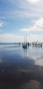 Wooden posts in sea against sky