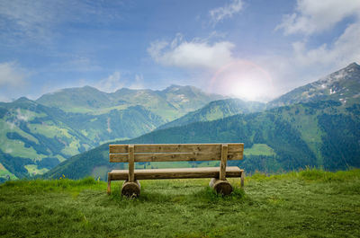 Bench on grassy field against mountains