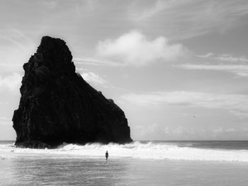 Silhouette people on rock by sea against sky