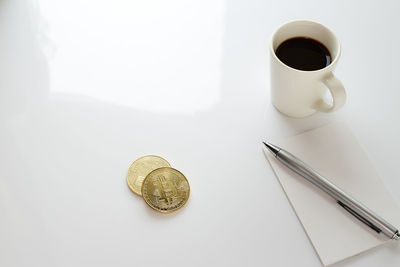 High angle view of coffee cup with bitcoins on white background