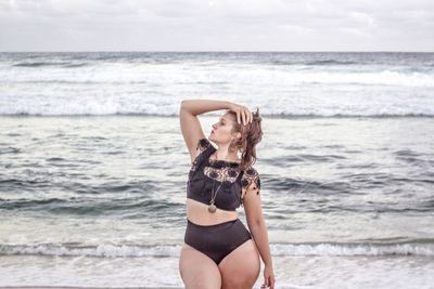 Portrait of young woman standing at beach against sky