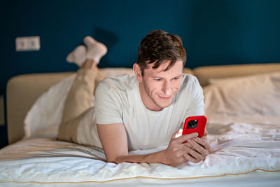 Man reading information in smartphone lying in bed at home in modern bedroom in evening.