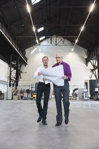 Two businessmen with plan walking in factory shop floor