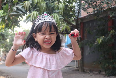 Portrait of girl clenching teeth while holding nail polish at yard