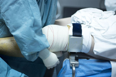 Close-up of doctor wrapping bandage on patient knee in operating room