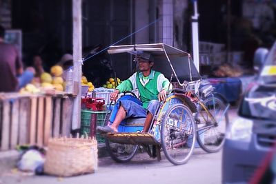 Driver sitting in rickshaw on road against market stall