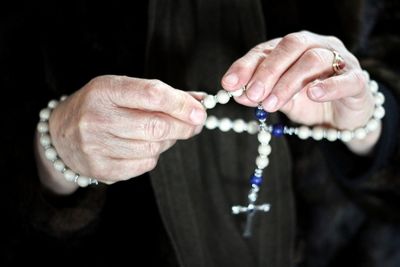 Midsection of woman holding bead necklace with cross pendant