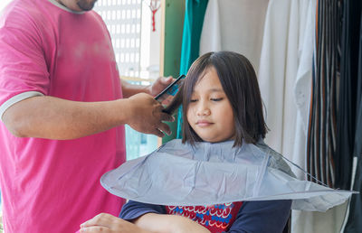 Asian child getting haircut at home from the father. young teenage girl.