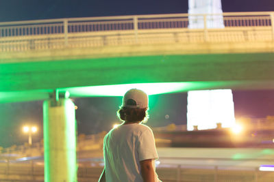 Rear view of man standing against illuminated bridge in city at night