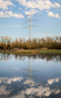 Reflection of electricity pylon on lake against sky