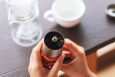 Closeup image of hands holding a stainless steel grinder with coffee beans to make drip coffee