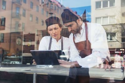 Owners using digital tablet in grocery store seen through glass window