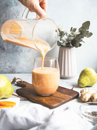 Hand with glass jug pours into a glass of fresh healthy carrot, pear, ginger smoothie chia seeds