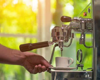 Close-up of person holding cup at espresso maker 