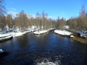 Frozen river by trees against sky