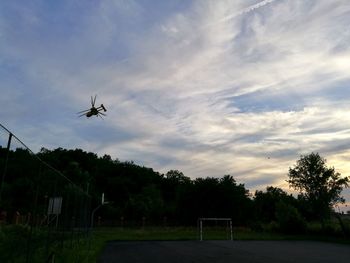 Airplane flying over trees against sky during sunset