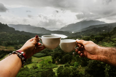 Midsection of man holding ice cream against mountains against sky