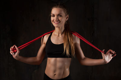 Portrait of young woman in bikini exercising with rope while standing against wall