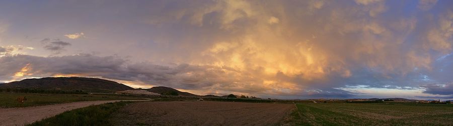 Road passing through field against cloudy sky