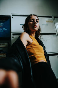 Low angle portrait of young woman standing by lockers