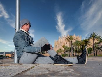 Man sitting by palm tree against sky