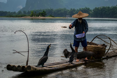 Fisherman feeding birds on paddleboard at river 