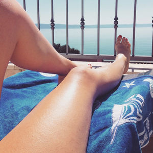 Low section of woman resting at balcony by sea during sunny day