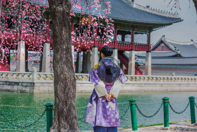 Rear view of woman standing by tree against building