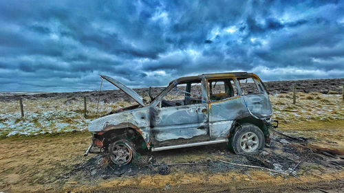 Abandoned car on land against sky