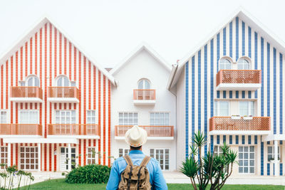 Back view of man with backpack standing at fence on costa nova and looking at colorful striped houses