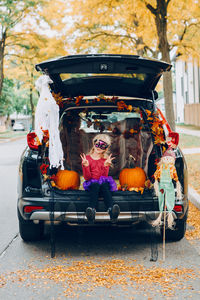 Trick or trunk. child girl celebrating halloween in trunk of car. kid with red pumpkins 