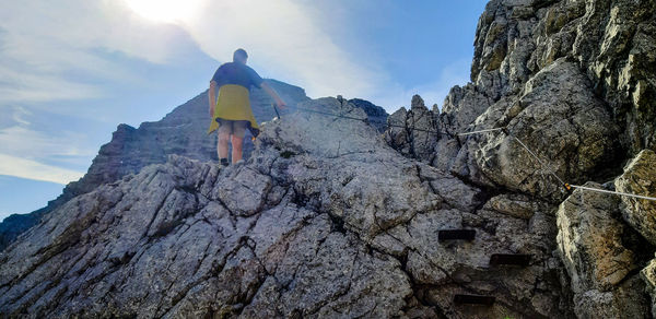 Rear view of man climbing on rock against sky