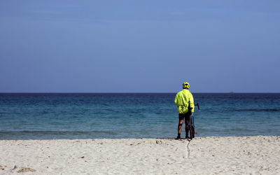 Rear view of man with bicycle standing at beach against clear sky