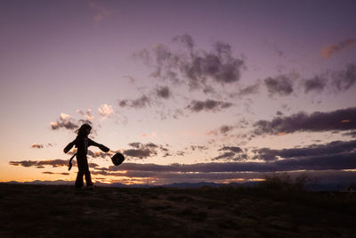 A young girl a twirls a halloween bucket on top of a hill at sunset