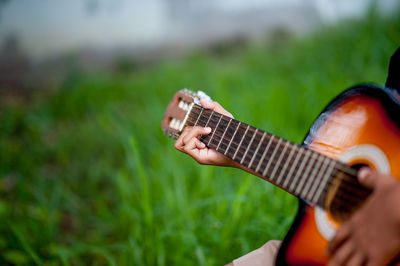 Cropped hand of person playing guitar over field