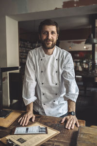 Portrait of confident chef standing by table in restaurant