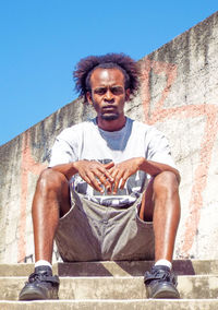 Full length portrait of young man sitting on steps against wall