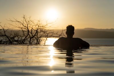 Silhouette man in swimming pool against sky during sunset
