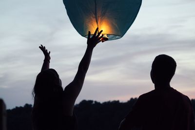 Woman flying lit paper lantern during sunset