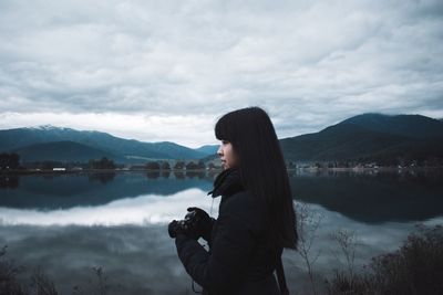 Side view of woman photographing lake against sky