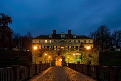 Illuminated footpath amidst buildings against sky at night