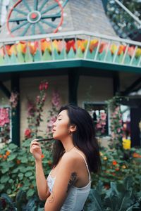 Side view of young woman standing by flowering plants