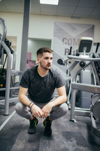 Young athlete squat sitting and thinking in a gym.