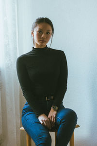 Portrait of young woman sitting on chair against wall