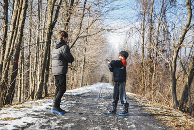 Two boys play fighting with sticks on a snowy trail in winter.