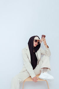 Young woman wearing sunglasses sitting on table against white background